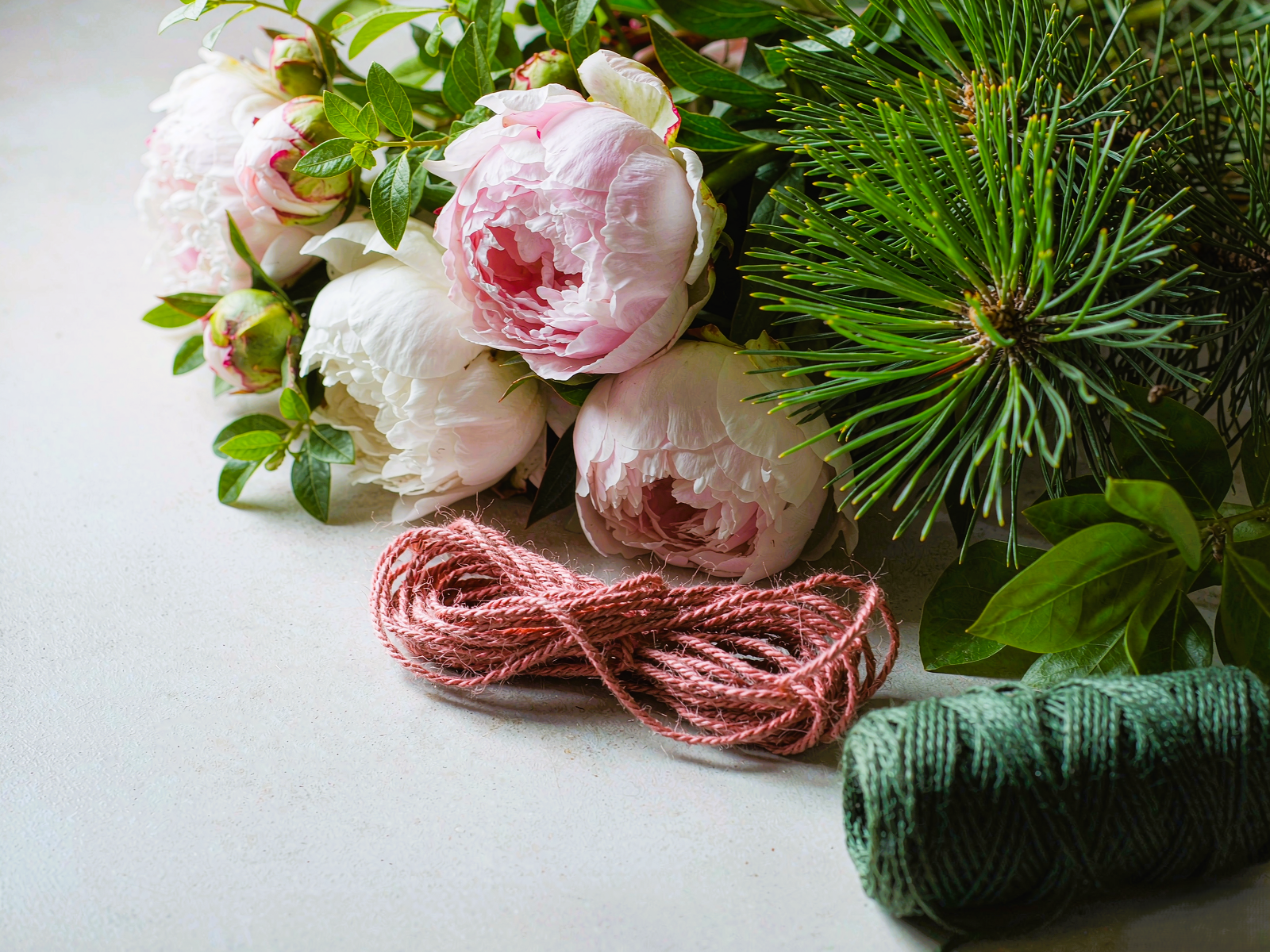 handwoven threads in peony pink and pine green beside fresh peonies and pine branches — Botanical series by TibetanTwist